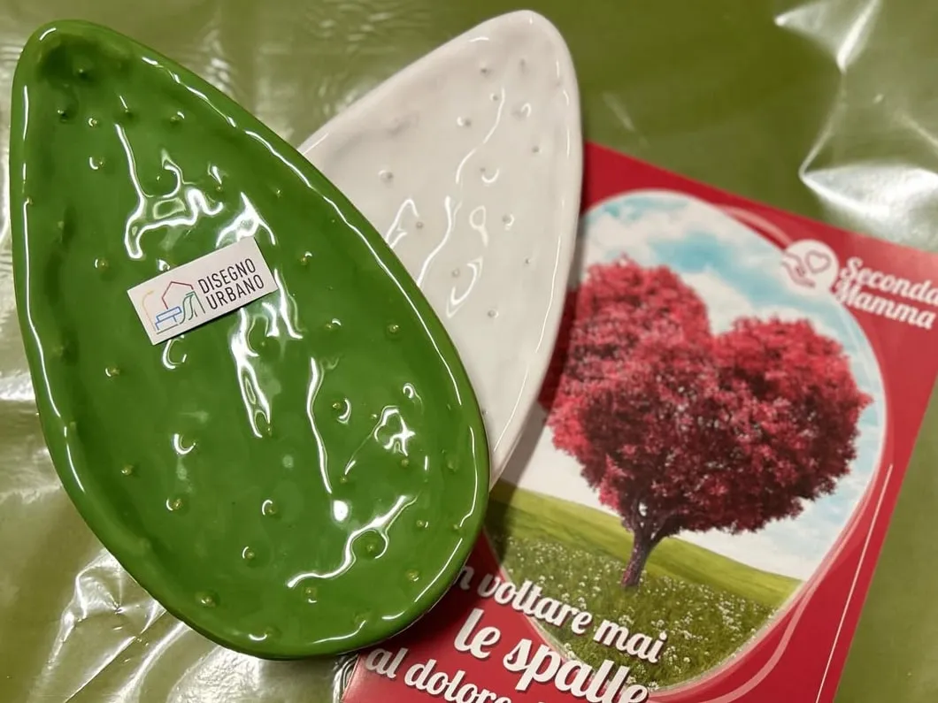 I piatti in ceramica a forma di pala di fico d'India, verde e bianco, della Pasqua 2024: sul piatto verde l'etichetta Disegno Urbano, accanto il biglietto di Seconda Mamma.